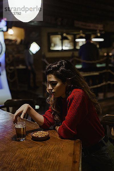 Traurige Mid Adult Frau mit Alkohol und Snacks auf dem Tisch sitzen im Restaurant
