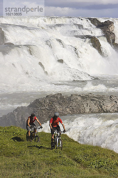 Island  Männer beim Mountainbiking  Wasserfall im Hintergrund