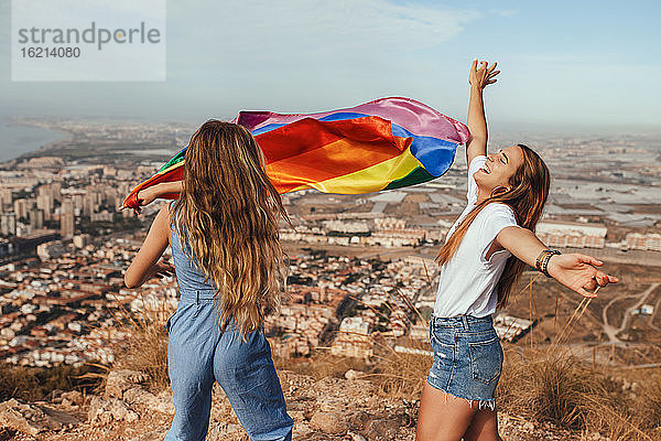 Zwei fröhliche junge Frauen mit einer LGBT-Flagge über der Küstenstadt Almeria  Spanien