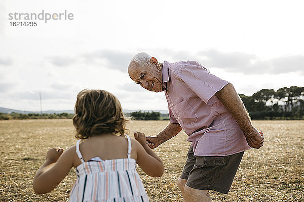 Großvater sieht seine Enkelin an  während er auf dem Land vor dem Himmel steht