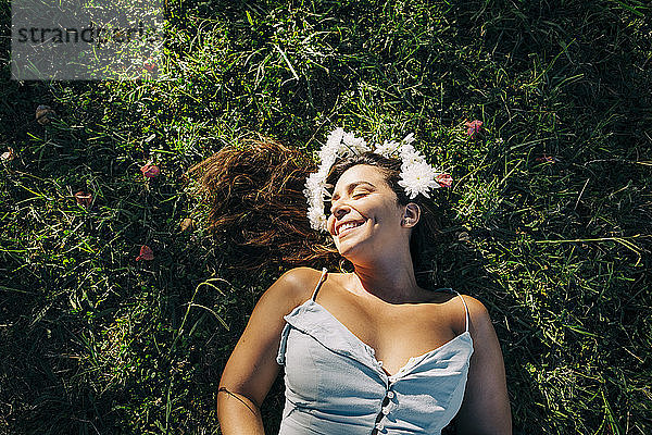 Junge Frau mit geschlossenen Augen entspannt sich auf einer Wiese im Park an einem sonnigen Tag