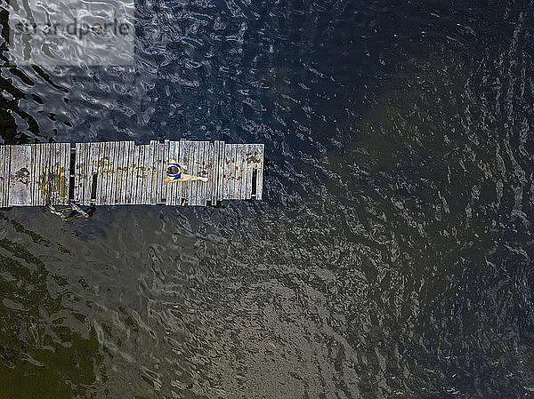 Luftaufnahme einer jungen Frau  die auf einem Steg am Seeufer spazieren geht