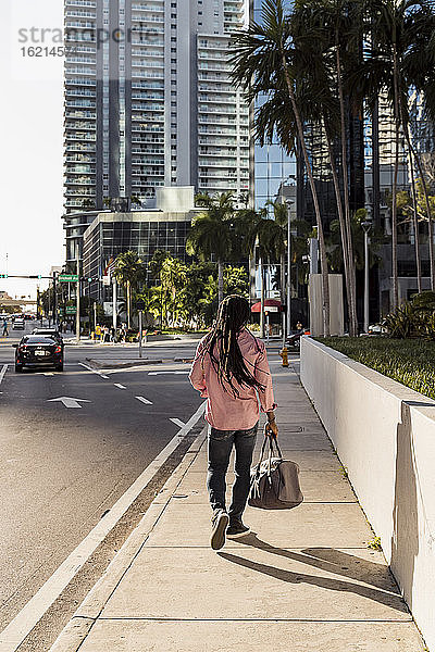 Afro-Mann mit Dreadlocks  der eine Tasche hält  während er auf dem Bürgersteig in Miami  Florida  USA  geht