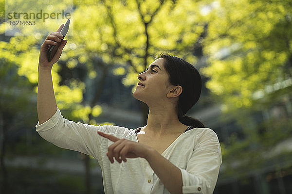 Junge Frau nimmt Selfie durch Smartphone gegen Bäume