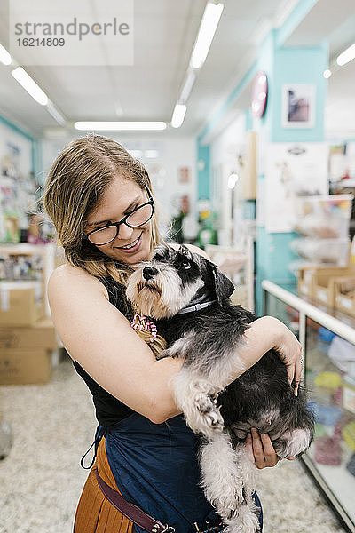 Glückliche Hundefrisörin  die einen Schnauzer umarmt  während sie in einem Haustiersalon steht