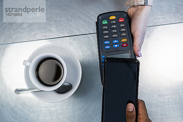 Kunde beim kontaktlosen Bezahlen mit seinem Smartphone in einem Café