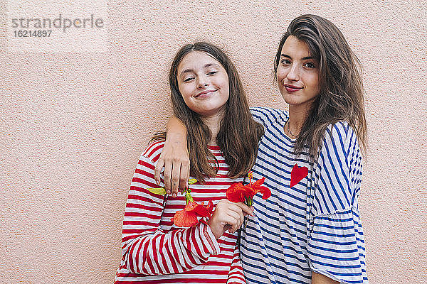 Lächelnde Schwestern  die Hibiskusblüten halten und an der Wand stehen
