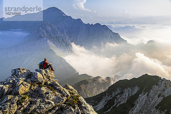 Mann sitzt und bewundert die Berglandschaft bei Sonnenaufgang in den Bergamasker Alpen  Italien