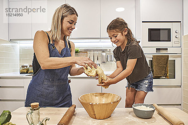 Lächelnde Mutter und Tochter kneten Pizzateig in der Küche zu Hause