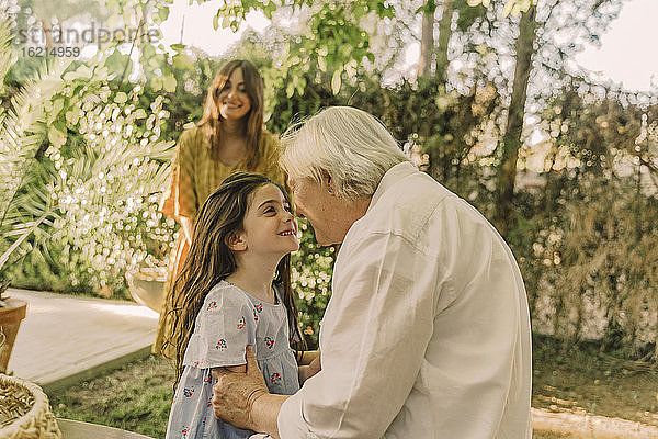 Lächelnde Frau betrachtet ein Mädchen  das mit seiner Großmutter im Garten spielt