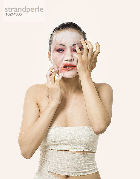 Nahaufnahme einer jungen Frau  die ihr Opern-Make-up verschmiert  während sie vor einem weißen Hintergrund steht