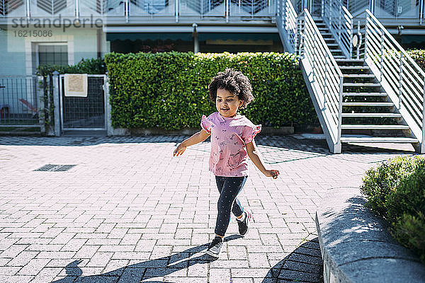 Baby-Mädchen mit lockigem Haar zu Fuß auf dem Gehweg während sonnigen Tag