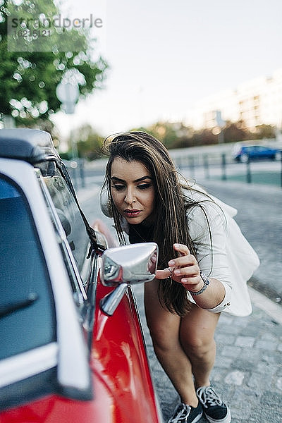 Junge Frau prüft ihr Aussehen im Spiegel des Autos