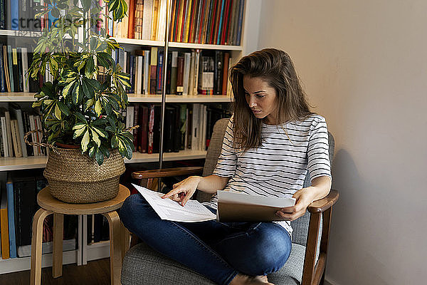 Geschäftsfrau liest ein Dokument  während sie auf einem Stuhl im Heimbüro sitzt