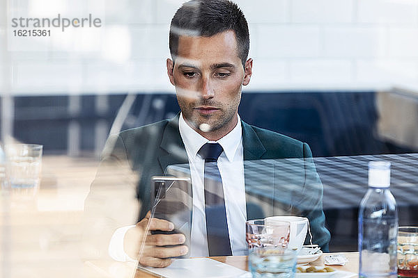 Geschäftsmann benutzt Smartphone in Café durch Glasfenster gesehen