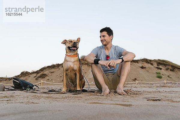 Mann mit seinem Hund genießt die Aussicht am Strand gegen den Himmel