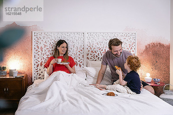 Glückliche Eltern mit Sohn beim Frühstück im Bett zu Hause