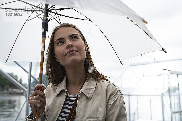 Nahaufnahme einer jungen Frau mit Regenschirm  die in der Stadt steht und nach oben schaut