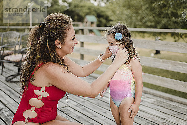 Mutter im Badeanzug  die ihrer Tochter eine schützende Gesichtsmaske anlegt