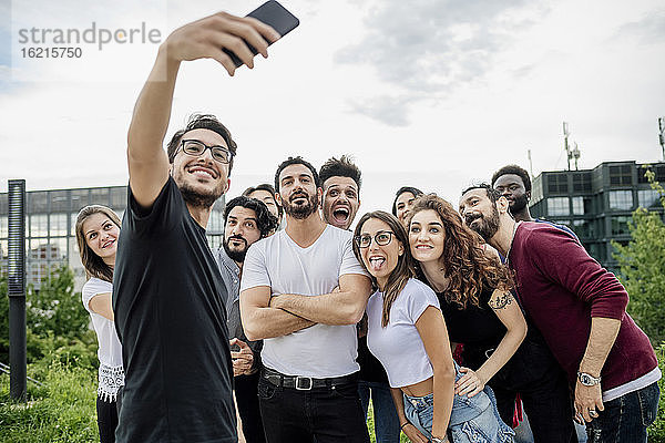 Fröhlicher Mann macht Selfie mit einer Gruppe von Freunden im Park gegen den Himmel