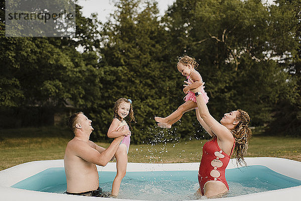 Glückliche Familie spielt in einem aufblasbaren Schwimmbad im Garten