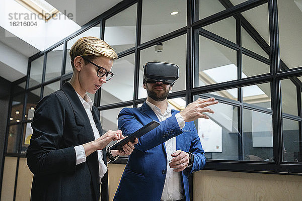 Eine Geschäftsfrau benutzt ein digitales Tablet  während sie einen Kollegen analysiert  der eine Virtual-Reality-Simulation im Büro erlebt