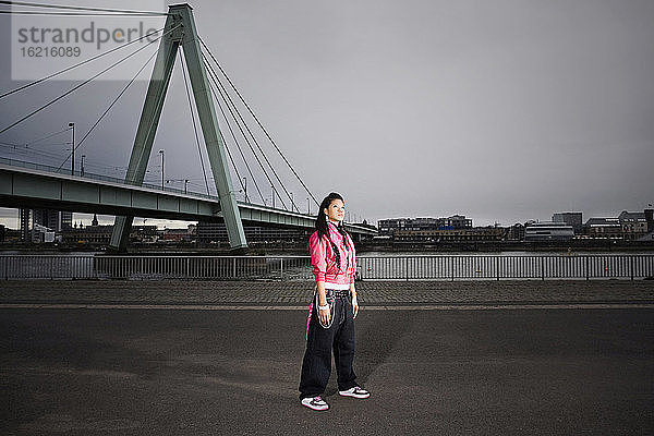 Deutschland  Köln  Junge Frau stehend  Brücke im Hintergrund