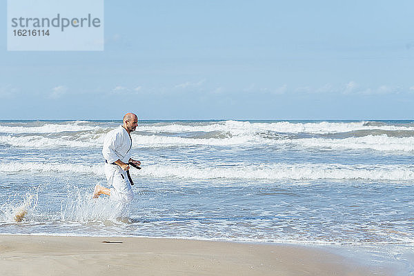 Älterer Mann in Badehose läuft am Strand gegen den Himmel an einem sonnigen Tag