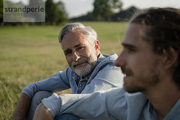 Älterer Vater mit erwachsenem Sohn auf einer Wiese in der Natur sitzend