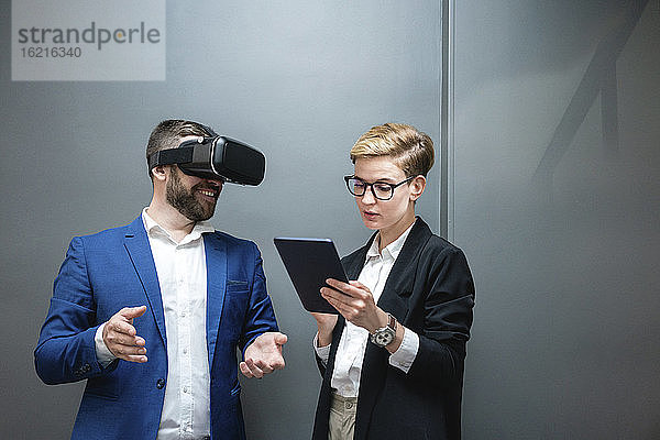 Eine Unternehmerin benutzt ein digitales Tablet  während sie einen Kollegen analysiert  der eine Virtual-Reality-Simulation im Büro erlebt