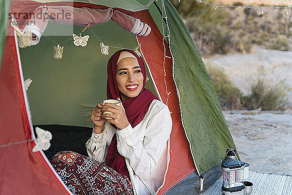 Lächelnde junge Touristin im Hijab in einem Zelt  die einen Becher hält