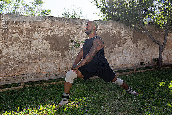 Kahler reifer Mann  der auf einer Wiese gegen eine Mauer im Hof trainiert