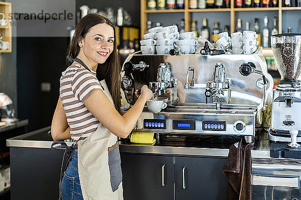 Glückliche weibliche Barista mit Kaffeemaschine im Café
