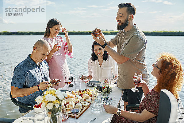 Freunde beim Abendessen an einem See  die ein Smartphone-Foto machen