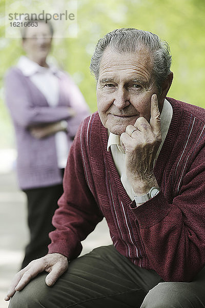 Deutschland  Köln  Porträt eines älteren Mannes im Park  während eine Frau im Hintergrund steht