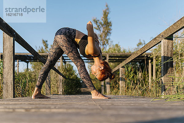 Junge Frau übt Yoga auf dem Pier auf dem Lande