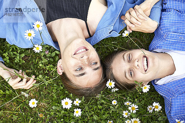 Nahaufnahme von fröhlichen Freundinnen  die bei Blumen auf einer Wiese im Garten liegen