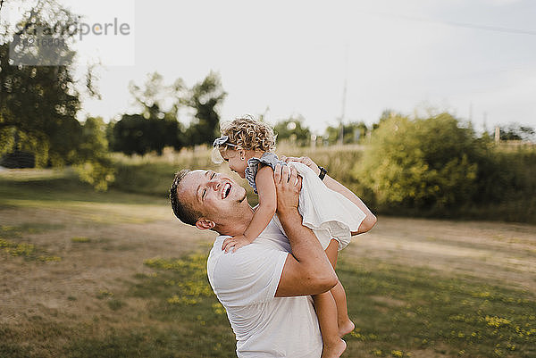 Glücklicher Vater trägt kleine Tochter auf einer Wiese