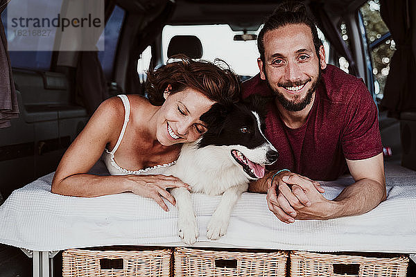 Lächelndes Paar mit Hund im Wohnmobil liegend