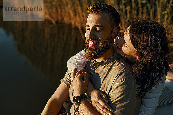 Glückliches  zärtliches Paar  das sich bei Sonnenuntergang an einem See umarmt