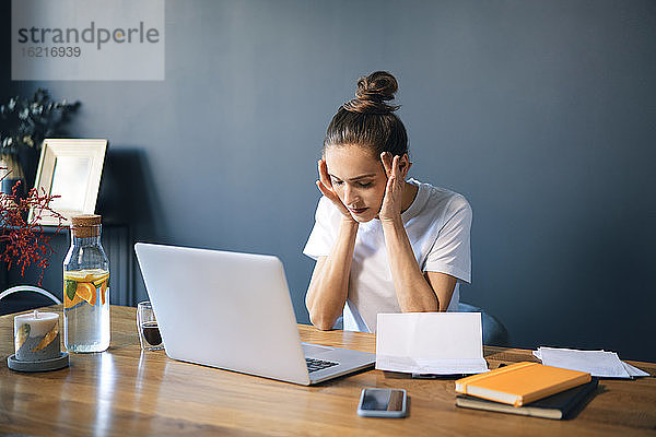 Weibliche Unternehmerin mit dem Kopf in den Händen sitzt am Schreibtisch gegen die Wand