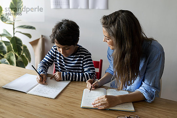 Junge Frau sitzt mit Schülerin bei den Hausaufgaben auf dem Tisch zu Hause