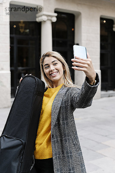 Junge Frau mit Geigenkasten macht Selfie in der Stadt