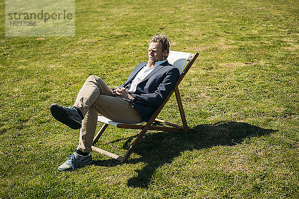 Entspannter Geschäftsmann auf einem Stuhl sitzend  während er an einem sonnigen Tag in den Park blickt