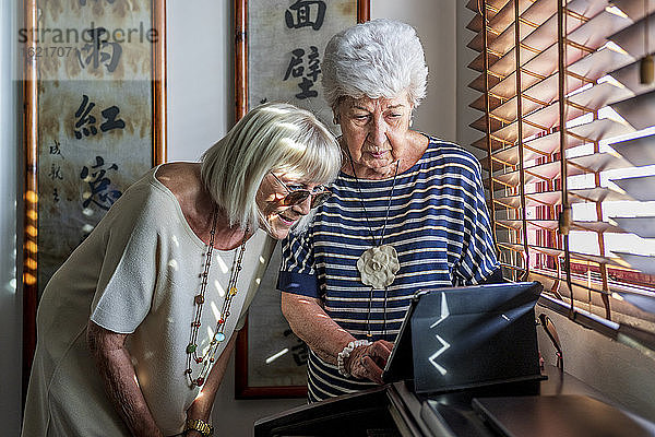 Ältere Freundinnen benutzen ein digitales Tablet am Klavier  während sie zu Hause stehen