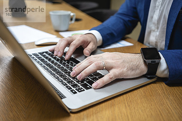 Nahaufnahme eines Geschäftsmannes beim Tippen auf einem Laptop an einem Schreibtisch in einem kreativen Coworking Space