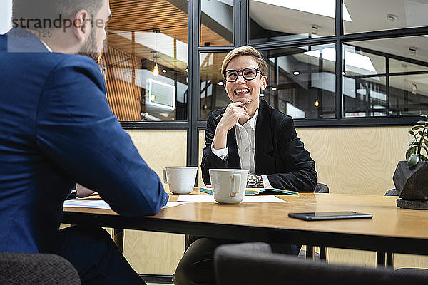 Lächelnde Geschäftsfrau  die während eines Vorstellungsgesprächs mit einer männlichen Führungskraft im Sitzungssaal sitzt