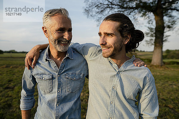 Glücklicher Vater und erwachsener Sohn umarmen sich auf einer Wiese auf dem Lande