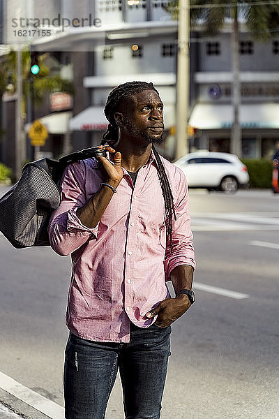 Nachdenklicher afroamerikanischer junger Mann mit Tasche auf der Straße in Miami  Florida  USA