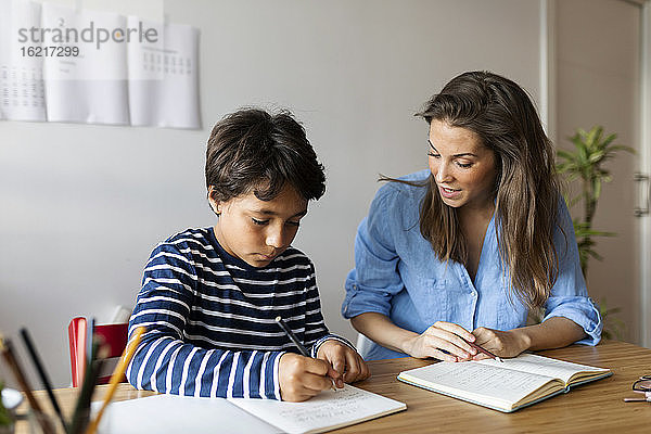 Weiblicher Tutor hilft Jungen beim Schreiben von Hausaufgaben auf dem Tisch zu Hause